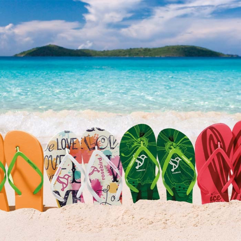 Plusieurs paires de tongs alignées sur une plage avec semelles personnalisées avec visuels imprimés visibles