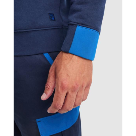 Zoom sur le poignet contrasté bleu d’un pull homme porté avec un pantalon de travail assorti, sans marquage visible.