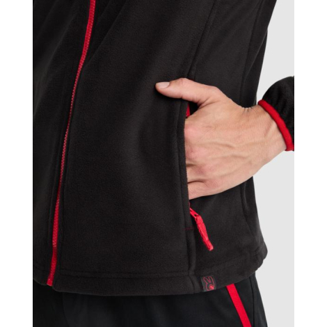 Zoom sur la poche latérale zippée et les détails contrastés rouges d’une veste unisexe en micropolaire noire sans marquage visib
