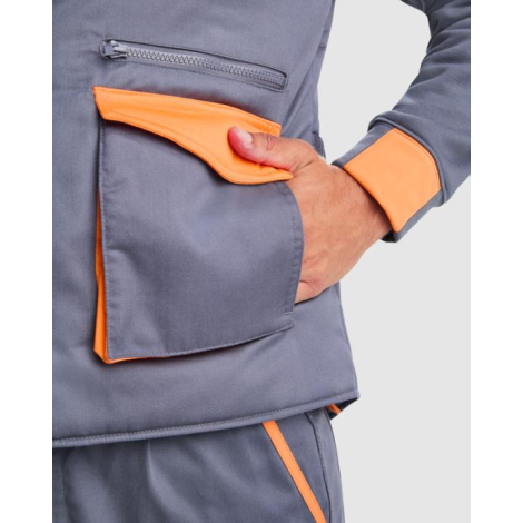 Zoom sur une poche basse à rabat et une poche zippée d’un gilet de travail gris avec détails orange, porté sans marquage visible