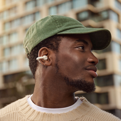 Homme portant des écouteurs sans fil blancs à oreille ouverte illustrés en situation d’utilisation, sans marquage apparent.