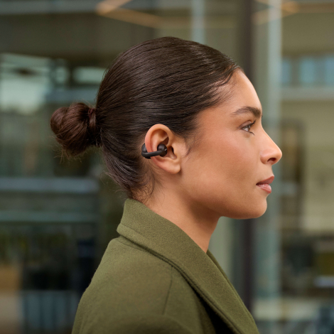 Femme portant des écouteurs sans fil noirs à oreille ouverte illustrés en situation d’utilisation, sans personnalisation visible