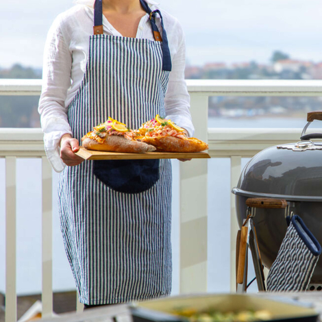 Femme portant un tablier de cuisine à rayures bleu foncé et blanches en tenant un plateau, sans personnalisation visible.