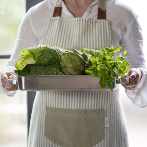Femme portant un tablier de cuisine à rayures claires en tenant un plateau de légumes, sans marquage apparent.
