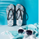 Tongs à motif illustré suspendues devant un fond bleu avec lunettes de soleil et textile au premier plan ; personnalisation appa
