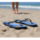 Paire de tongs à motif bleu posée sur le sable en bord de mer, avec personnalisation visible sur la surface des semelles.