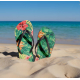 Paire de tongs à motif tropical plantée dans le sable face à la mer, avec personnalisation visible sur la surface des semelles. Paire de tongs à motif tropical plantée dans le sable face à la mer, avec personnalisation visible sur la surface des semelles.