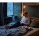 Homme utilisant un ordinateur portable sur un lit avec ventilateur sans pales allumé en arrière-plan, sans marquage visible. Homme utilisant un ordinateur portable sur un lit avec ventilateur sans pales allumé en arrière-plan, sans marquage visible.