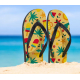 Paire de tongs à motif estival plantée dans le sable face à la mer, avec personnalisation visible sur la surface des semelles.