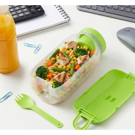 Boîte à lunch remplie de nourriture dans un environnement de bureau avec couvercle ouvert et cuillère-fourchette posée à côté, s