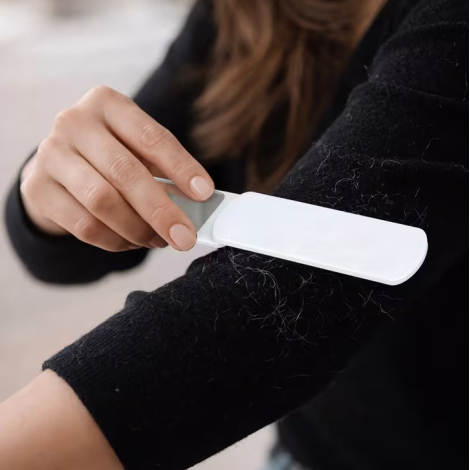 Femme utilisant la surface textile de la brosse à peluches sur la manche d’un vêtement foncé.