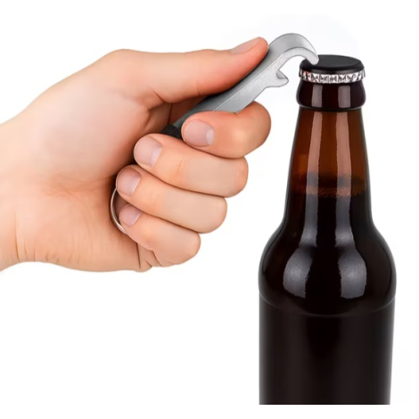 Porte-clés décapsuleur 3 en 1 utilisé pour ouvrir une bouteille, tenu en main et engagé sous la capsule du bouchon.