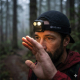 Homme portant la lampe frontale allumée en extérieur forestier, sans personnalisation visible sur la face avant du boîtier. Homme portant la lampe frontale allumée en extérieur forestier, sans personnalisation visible sur la face avant du boîtier.