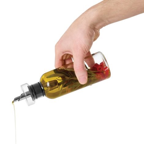 Détail d’une bouteille en verre remplie d’huile aromatisée, tenue en main et inclinée pour le service à l’aide du bec verseur mé