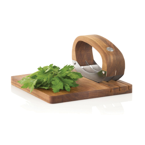 Ensemble hachoir avec planche présenté avec des herbes fraîches déposées sur la planche.
