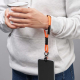 Personne tenant une tasse avec une dragonne orange équipée d’un câble de charge intégré et d’un smartphone suspendu, avec marqua Personne tenant une tasse avec une dragonne orange équipée d’un câble de charge intégré et d’un smartphone suspendu, avec marqua
