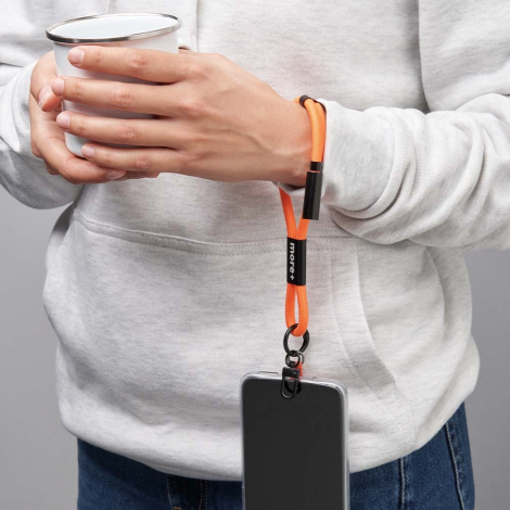 Personne tenant une tasse avec une dragonne orange équipée d’un câble de charge intégré et d’un smartphone suspendu, avec marqua