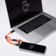 Ordinateur portable et smartphone reliés par le câble de charge intégré d’une dragonne orange. Ordinateur portable et smartphone reliés par le câble de charge intégré d’une dragonne orange.