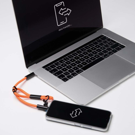 Ordinateur portable et smartphone reliés par le câble de charge intégré d’une dragonne orange.