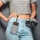 Femme portant un smartphone suspendu à un cordon bicolore jaune et noir en bandoulière tout en tenant un appareil photo sans per Femme portant un smartphone suspendu à un cordon bicolore jaune et noir en bandoulière tout en tenant un appareil photo sans per