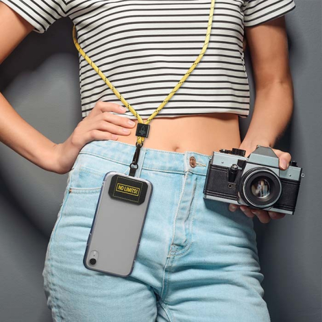 Femme portant un smartphone suspendu à un cordon bicolore jaune et noir en bandoulière tout en tenant un appareil photo sans per
