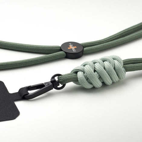 Gros plan sur un cordon vert avec nœud contrasté, mousqueton noir et plaque de fixation, accompagné d’un élément de réglage circ