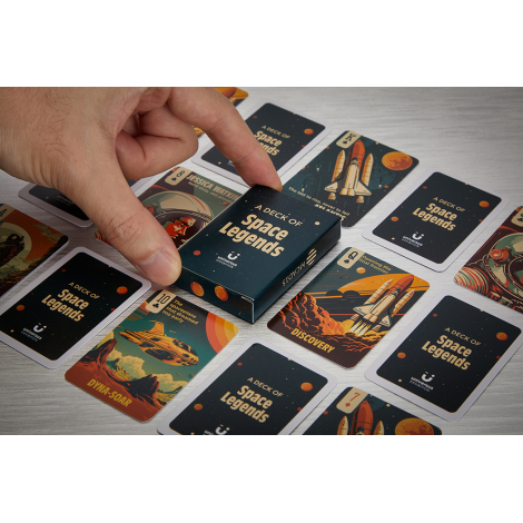 Main manipulant un étui de jeu de cartes personnalisé posé au milieu de cartes illustrées présentant différents graphismes visib
