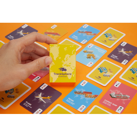 Main tenant un étui de jeu de cartes personnalisé devant plusieurs cartes illustrées avec graphismes colorés visibles