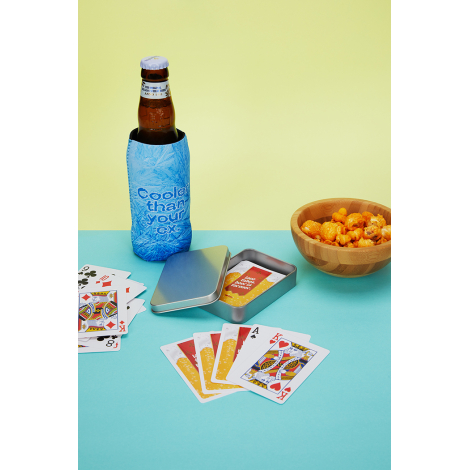 Jeu de cartes personnalisé présenté dans un contexte de détente avec cartes étalées, boîte métallique ouverte et étui illustré c