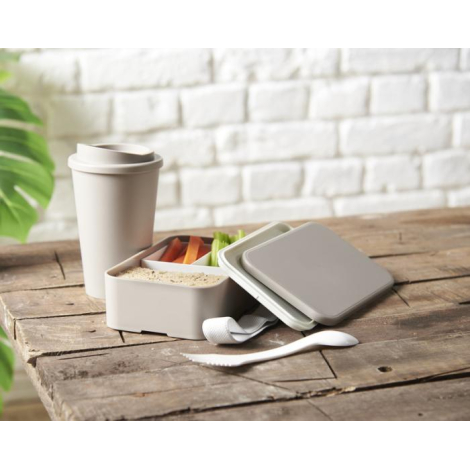 Boîte à déjeuner ouverte dans un environnement de repas, avec des crudités visibles à l’intérieur et le couvercle posé à côté.