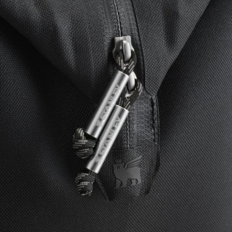 Gros plan sur les curseurs métalliques de la fermeture zippée et la tirette siglée du sac noir.