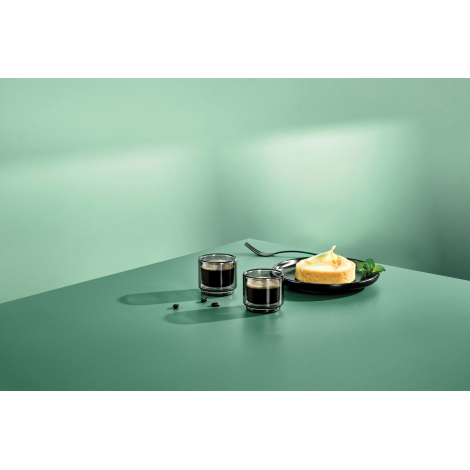 Mise en situation du lot de deux tasses à expresso remplies de café, présentées sur une table à côté d'une assiette de dessert, 