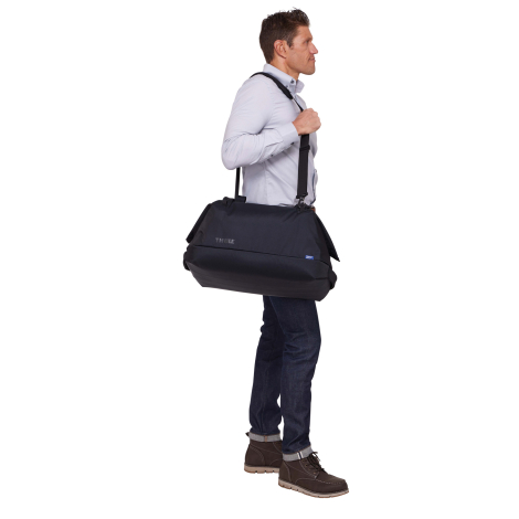 Homme portant le sac de voyage à l'épaule grâce à la bandoulière, sans personnalisation visible.