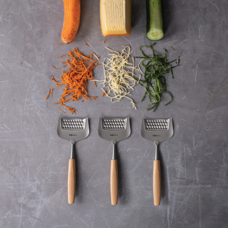 Trois tranchettes à fromage alignées sous différents légumes et fromages râpés, sans marquage visible.