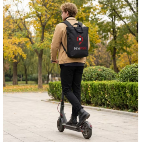 Homme circulant sur une trottinette avec le sac porté comme sac à dos et une personnalisation visible sur la face arrière.