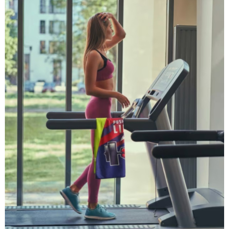 Femme courant sur un tapis de course avec une serviette R-PET Quick Dry comportant une personnalisation visible sur une face.