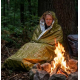 Homme utilisant le sac de couchage thermique d'urgence alors qu'il est assis près d'un feu de camp. Homme utilisant le sac de couchage thermique d'urgence alors qu'il est assis près d'un feu de camp.