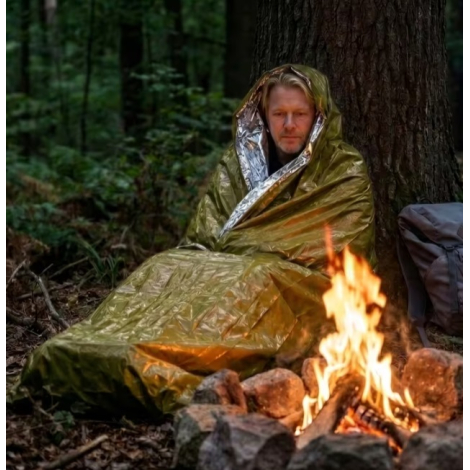 Homme utilisant le sac de couchage thermique d'urgence alors qu'il est assis près d'un feu de camp.