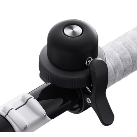 Sonnette de vélo noire installée sur un guidon, mettant en évidence son système de fixation et son bouton métallique supérieur.