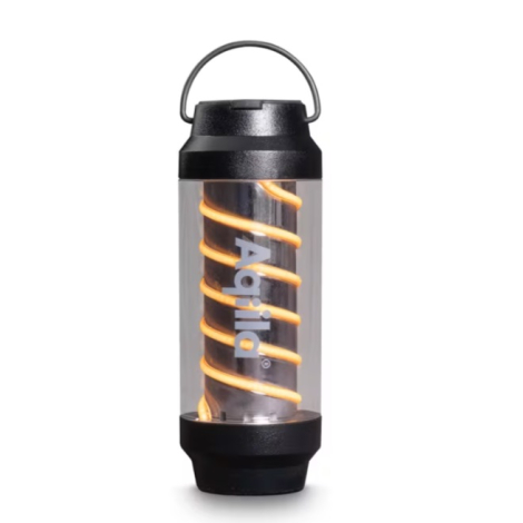 Lampe de camping présentée de face sur fond clair avec filament lumineux en spirale visible à travers le corps transparent et ma