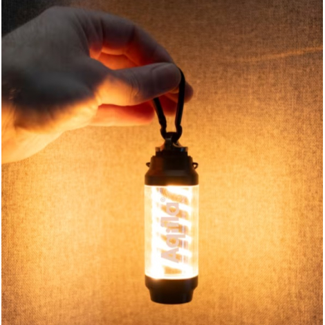 Lampe allumée suspendue par un mousqueton et tenue à la main dans un environnement sombre, laissant apparaître une personnalisat