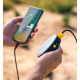 Lampe et batterie externe tenues en main et reliées à un smartphone en cours de charge dans un environnement extérieur.