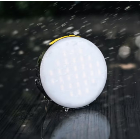 Lampe allumée présentée sous la pluie, mettant en avant sa face lumineuse circulaire dans un environnement humide.