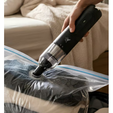 Mini aspirateur souffleur utilisé avec un embout de mise sous vide sur un sac de rangement, sans personnalisation visible.