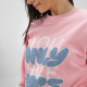 Gros plan sur une femme portant un sweat à col rond rose avec un marquage en relief visible sur le devant.