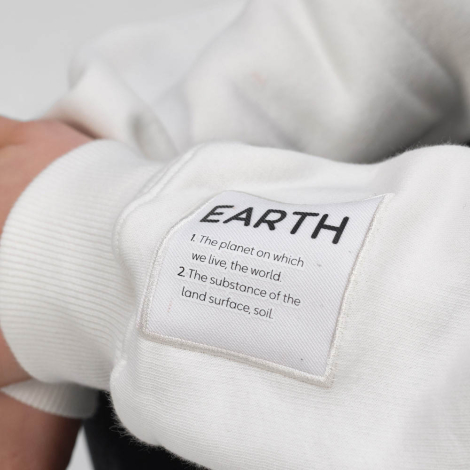Gros plan sur le bas de la manche d'un sweat à col montant avec demi-zip, avec un écusson textile cousu visible.
