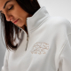 Gros plan sur un sweat à col montant avec demi-zip porté par une femme, avec une broderie visible sur la poitrine. Gros plan sur un sweat à col montant avec demi-zip porté par une femme, avec une broderie visible sur la poitrine.