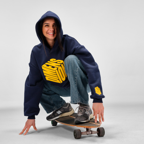 Femme portant un sweat à capuche oversize bleu marine avec un marquage visible sur le devant et en bas de la manche gauche, accr