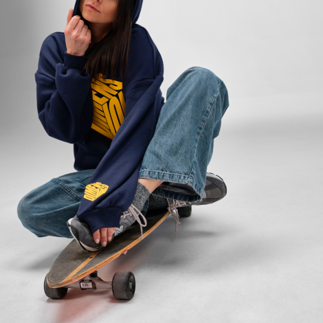 Femme portant un sweat à capuche oversize bleu marine avec un marquage visible sur le devant et en bas de la manche gauche.