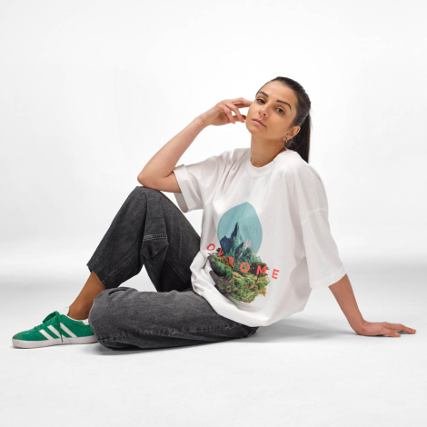Femme assise portant un t-shirt oversize blanc avec un marquage visible au centre de la poitrine.